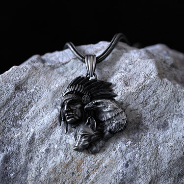 Oxidized sterling silver Native American pendant with chief, eagle, and wolf designs, resting on a textured gray rock.