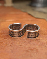 Oxidized sterling silver spell ring showing the double-loop construction and ancient glyphs, resting on a tan leather background.