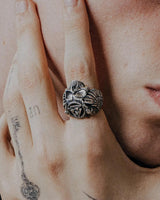 Silver Valknut Skull Ring with detailed wings shown on a man's tattooed finger for a lifestyle and scale reference.