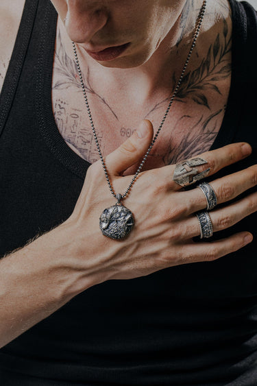 Man with tattoos wearing a Spartan helmet ring and wolf pendant, showcasing its edgy, military-inspired style for men.
