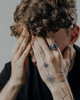 A man wearing the silver Viking Warrior ring on his finger, highlighting its size and bold style alongside hand tattoos.