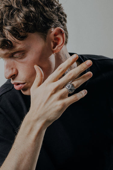 Close-up of a man's hand touching his face, highlighting the handcrafted silver owl ring worn as a statement piece of jewelry.