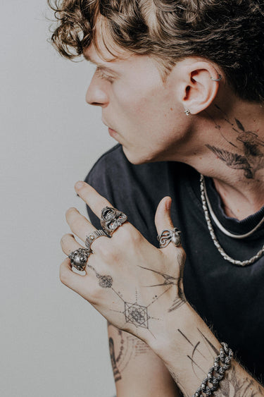 A man with hand tattoos wearing the Silver Octopus Ring on his index finger, showcasing its bold, gothic style with other rings.