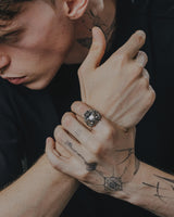 A man wearing the large sterling silver horned skull ring, showcasing its scale and statement appeal as part of a modern, tattooed look.