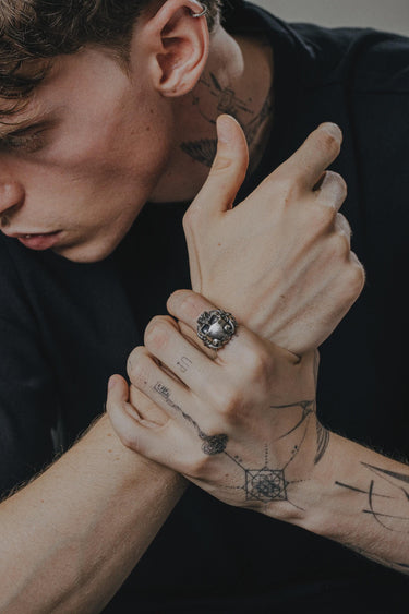 A man wearing the large sterling silver horned skull ring, showcasing its scale and statement appeal as part of a modern, tattooed look.