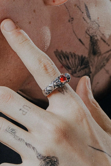 Gothic silver bat ring with red gemstone worn on a finger, showcasing its scale and alternative style against tattooed skin.