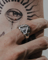 Silver evil eye hand ring worn on a finger, showing the detailed protective eye design against a sun tattoo.