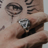 Silver evil eye hand ring worn on a finger, showing the detailed protective eye design against a sun tattoo.