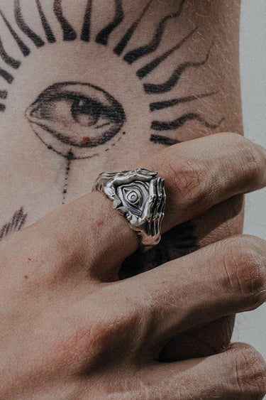 Silver evil eye hand ring worn on a finger, showing the detailed protective eye design against a sun tattoo.