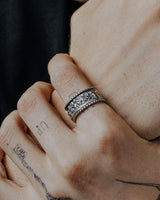 A sterling silver Last Supper Ring worn on a man's tattooed finger, showing the ring's oxidized detail and texture.