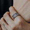 A sterling silver Last Supper Ring worn on a man's tattooed finger, showing the ring's oxidized detail and texture.
