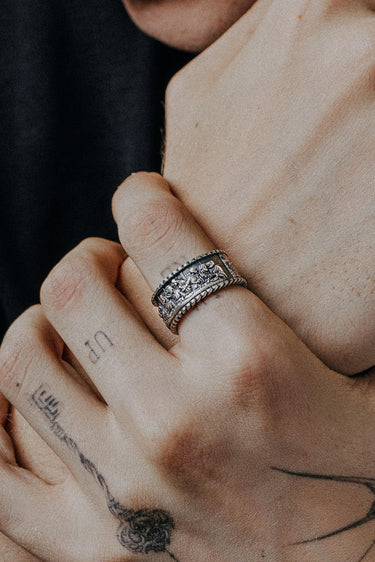 A sterling silver Last Supper Ring worn on a man's tattooed finger, showing the ring's oxidized detail and texture.