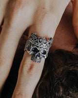 A close-up of the gothic crown skull ring worn on a person's finger, showcasing the intricate side profile and band details.