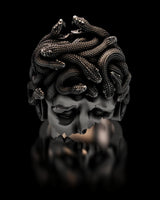 Silver Medusa ring with detailed, oxidized snakes for hair, shown on a reflective black background for a luxury feel.