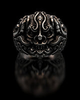 Sterling silver Oni mask ring with intricate carvings and oxidized finish shown in a studio shot on a reflective black background.