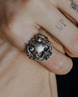 Handcrafted silver horned skull ring with an oxidized finish, worn on a tattooed finger to show its bold, gothic style.