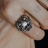 Handcrafted silver horned skull ring with an oxidized finish, worn on a tattooed finger to show its bold, gothic style.