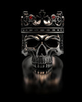 Sterling silver Skull King Ring with a detailed crown and red stones, shown front-on with a reflection on a black surface.