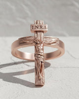 Rose gold plated crucifix ring with INRI inscription casting shadow on white marble surface religious jewelry
