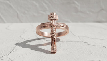 Rose gold plated crucifix ring with INRI inscription casting shadow on white marble surface religious jewelry