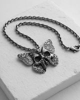 Handcrafted butterfly skull necklace with oxidized finish displayed on white marble jewelry stand