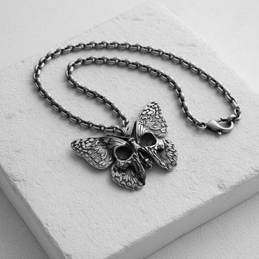 Handcrafted butterfly skull necklace with oxidized finish displayed on white marble jewelry stand