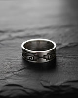 Side view of handcrafted Aztec ring on dark wood showing oxidized finish and traditional pattern depth