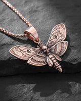 Rose gold plated Death Head Moth Pendant with an intricate skull design, displayed at an angle on a textured dark stone.