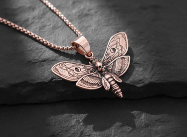 Rose gold plated Death Head Moth Pendant with an intricate skull design, displayed at an angle on a textured dark stone.
