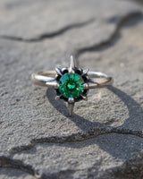 925 sterling silver starburst ring with emerald green stone and spike prongs on textured stone surface