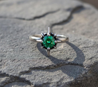 925 sterling silver starburst ring with emerald green stone and spike prongs on textured stone surface