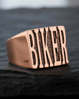 Rose gold plated biker ring showing detailed letter texture and premium finish on dark slate background
