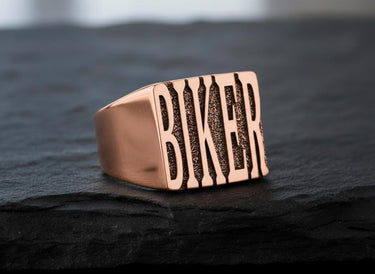 Rose gold plated biker ring showing detailed letter texture and premium finish on dark slate background
