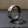 Modern geometric silver ring with oxidized matte segments and a polished accent link, standing on a dark slate surface.