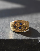 Gold Vermeil Sapphire Crater Ring with bezel-set blue sapphires, a unique signet ring for men displayed on a stone ledge.