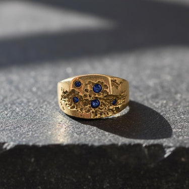 Gold Vermeil Sapphire Crater Ring with bezel-set blue sapphires, a unique signet ring for men displayed on a stone ledge.