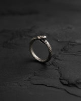 Side angle of oxidized sterling silver ouroboros ring on dark slate surface showing dimensional metalwork and gothic styling