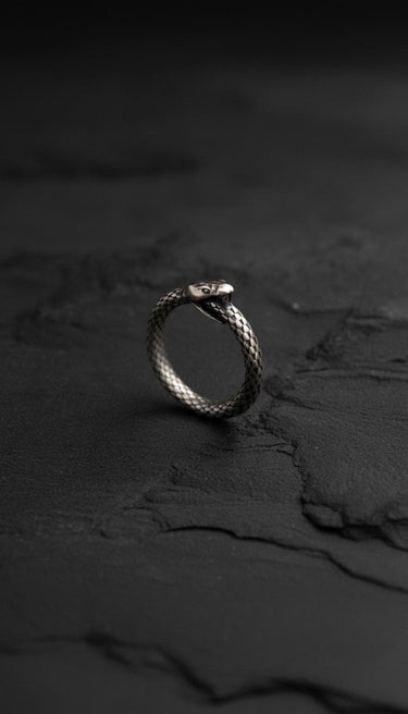 Side angle of oxidized sterling silver ouroboros ring on dark slate surface showing dimensional metalwork and gothic styling