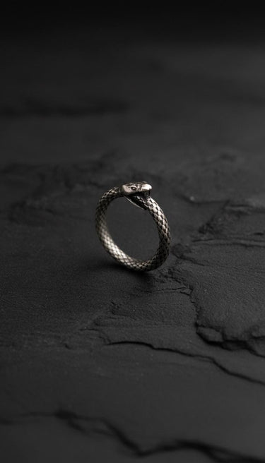 Close-up view of silver snake ring on dark stone surface highlighting serpent head and tail craftsmanship