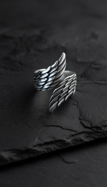 Side view of handcrafted angel wings ring on dark slate background highlighting oxidized finish and band details