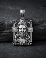 Sterling silver Christian cross pendant with three-dimensional relief work displayed on textured black stone