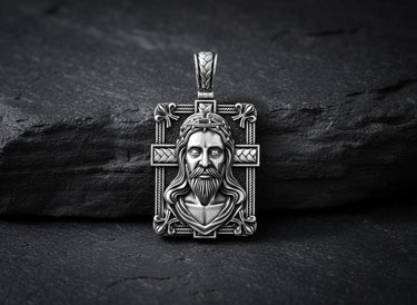 Sterling silver Christian cross pendant with three-dimensional relief work displayed on textured black stone