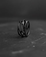 Black rhodium plated sterling silver parametric ring with organic web design displayed on dark stone surface