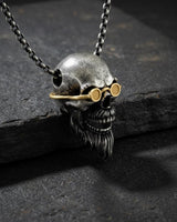 Silver bearded skull pendant with gold vermeil goggles shown at an angle on a dark, textured slate surface for a dramatic look.