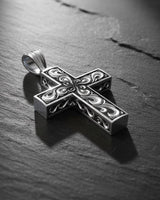 Side angle view of handcrafted cross pendant showing dimensional filigree scrollwork and oxidized silver finish