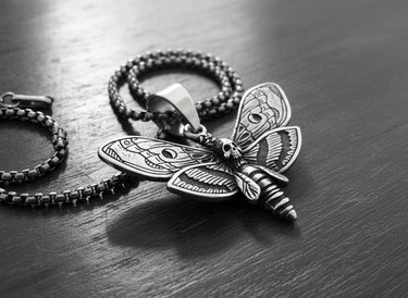 Black and white photo of the 925 sterling silver skull moth pendant, highlighting its 3D texture and craftsmanship on a wood surface.