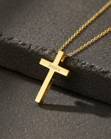 Personalized cross necklace in 18k gold vermeil with the name 'Jessica' engraved, resting on a dark textured stone.