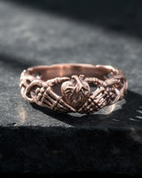 Gothic claddagh ring in rose gold tone showing skeleton hands cradling heart design on textured concrete background