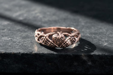 Gothic claddagh ring in rose gold tone showing skeleton hands cradling heart design on textured concrete background