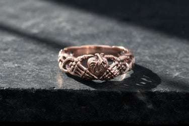 Rose gold plated silver Claddagh ring showing skeletal hand details and Irish symbolism on dark slate background